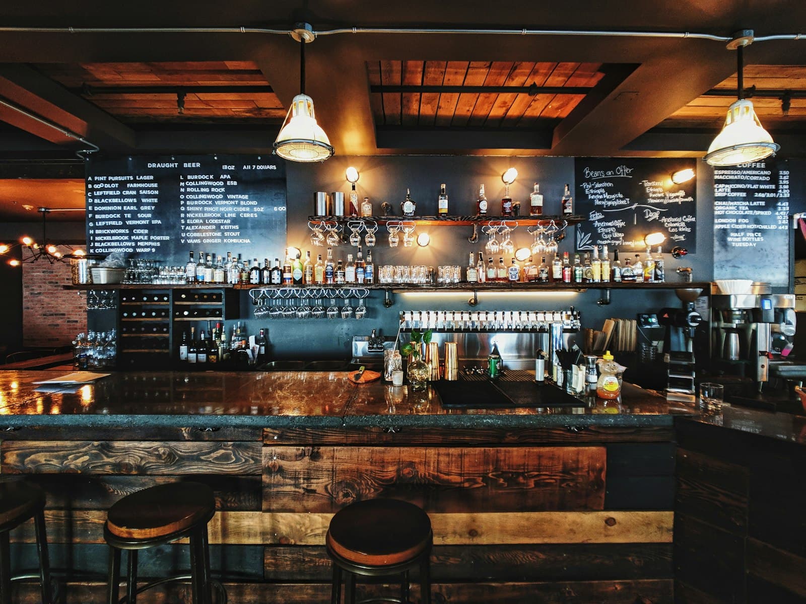 Warmly lit wooden bar lined with bottles and chalkboard menus