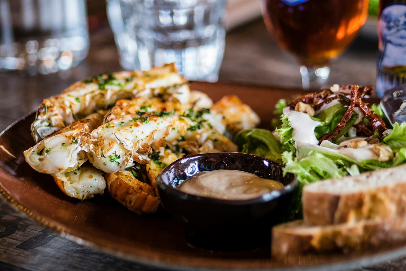 Rustic plate of wood-fired food with a dipping sauce and fresh greens on a dark table