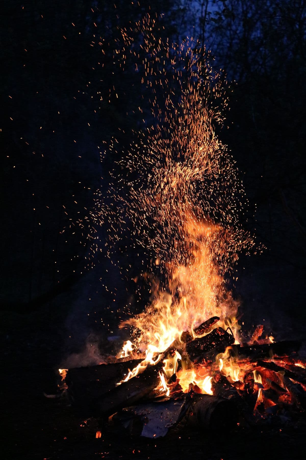 Wood fire burning at night with bright orange sparks rising into the dark