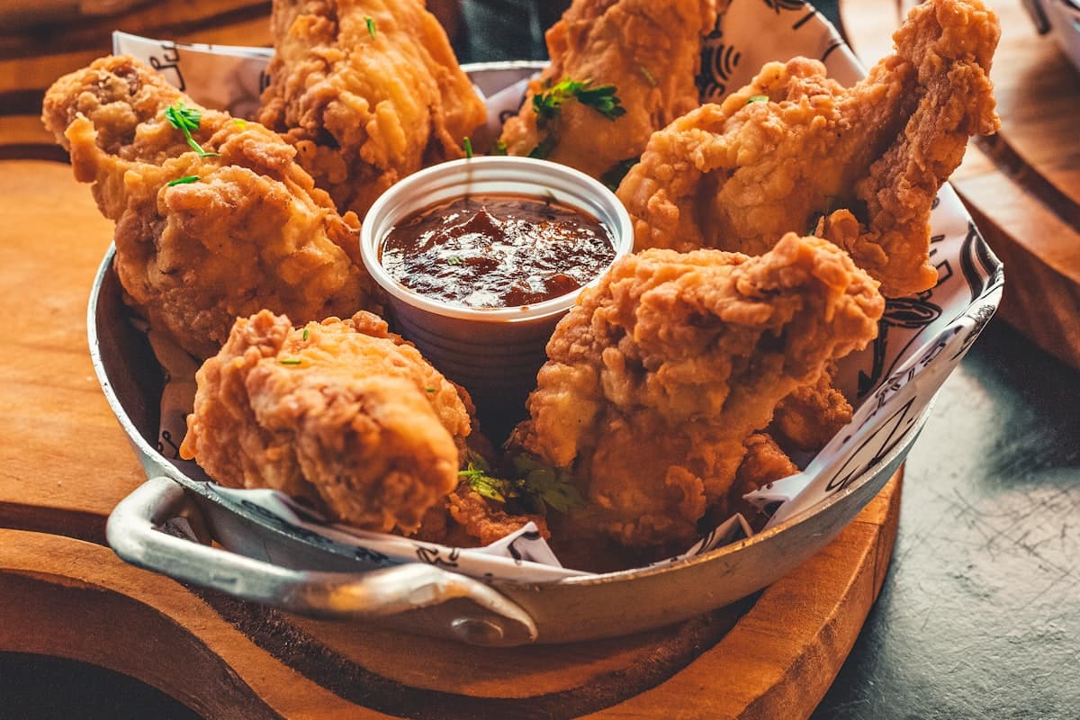 Basket of crispy fried chicken with a ramekin of barbecue sauce on a dark wooden board