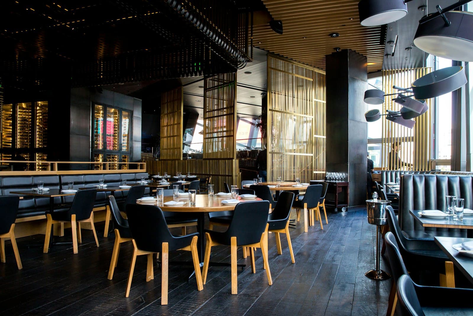 Moody restaurant dining room with dark wood floors, leather banquettes, and brass screens