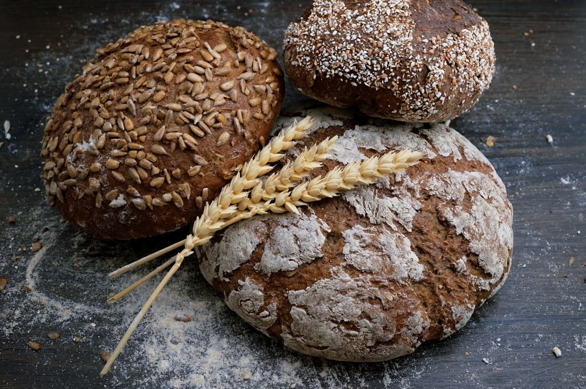 Rustic loaves of freshly baked bread dusted with flour on a dark wooden table with stalks of wheat
